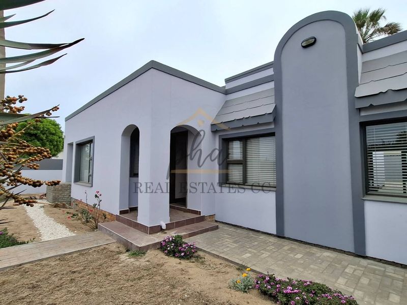 A well-maintained front facade featuring a covered entrance porch, paved walkway, and modern grey exterior paint finish with aluminium window frames.