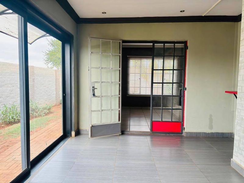 An empty living area featuring large sliding glass doors, tiled flooring, and a secure metal entrance gate leading to an adjacent room.