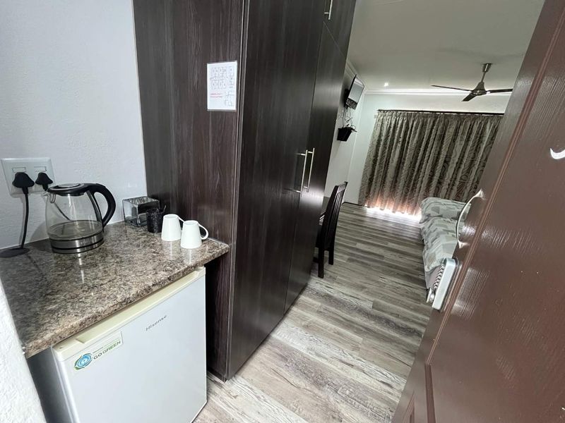 A bedroom featuring laminate flooring, a ceiling fan, and a compact kitchenette area with built-in cupboards and a granite countertop.