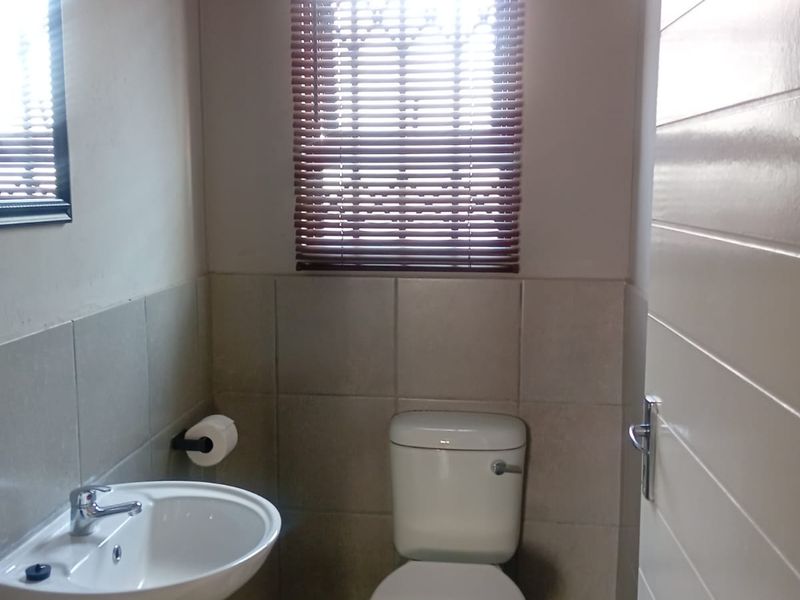 A clean and functional guest bathroom featuring a pedestal basin, toilet, and neutral wall tiling with fitted venetian blinds.