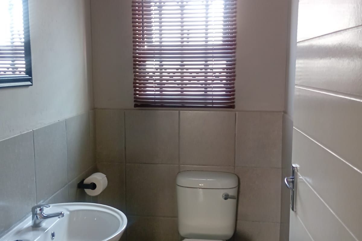 A clean and functional guest bathroom featuring a pedestal basin, toilet, and neutral wall tiling with fitted venetian blinds.