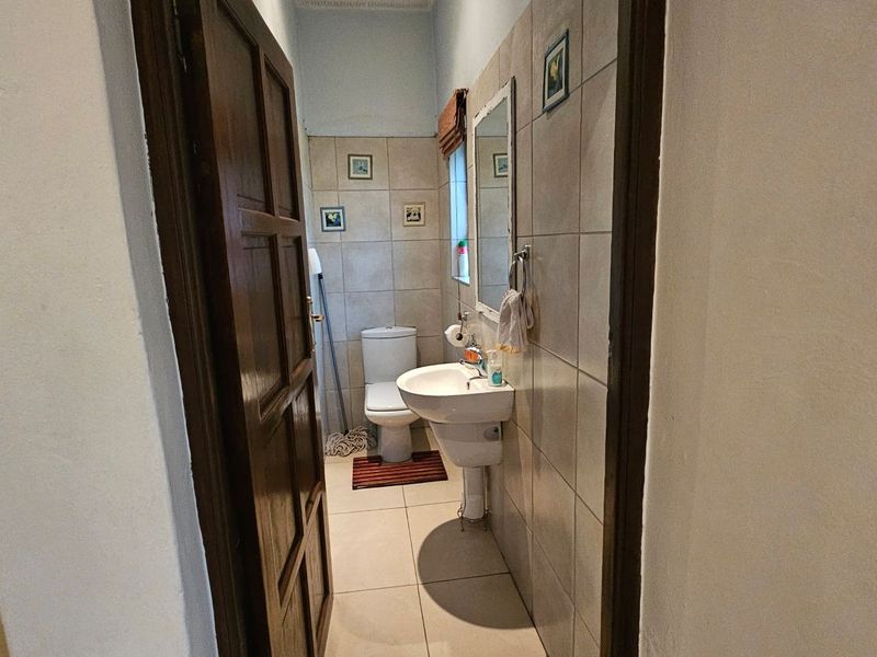 A compact bathroom featuring tiled walls and flooring, equipped with a pedestal basin and a standard toilet.