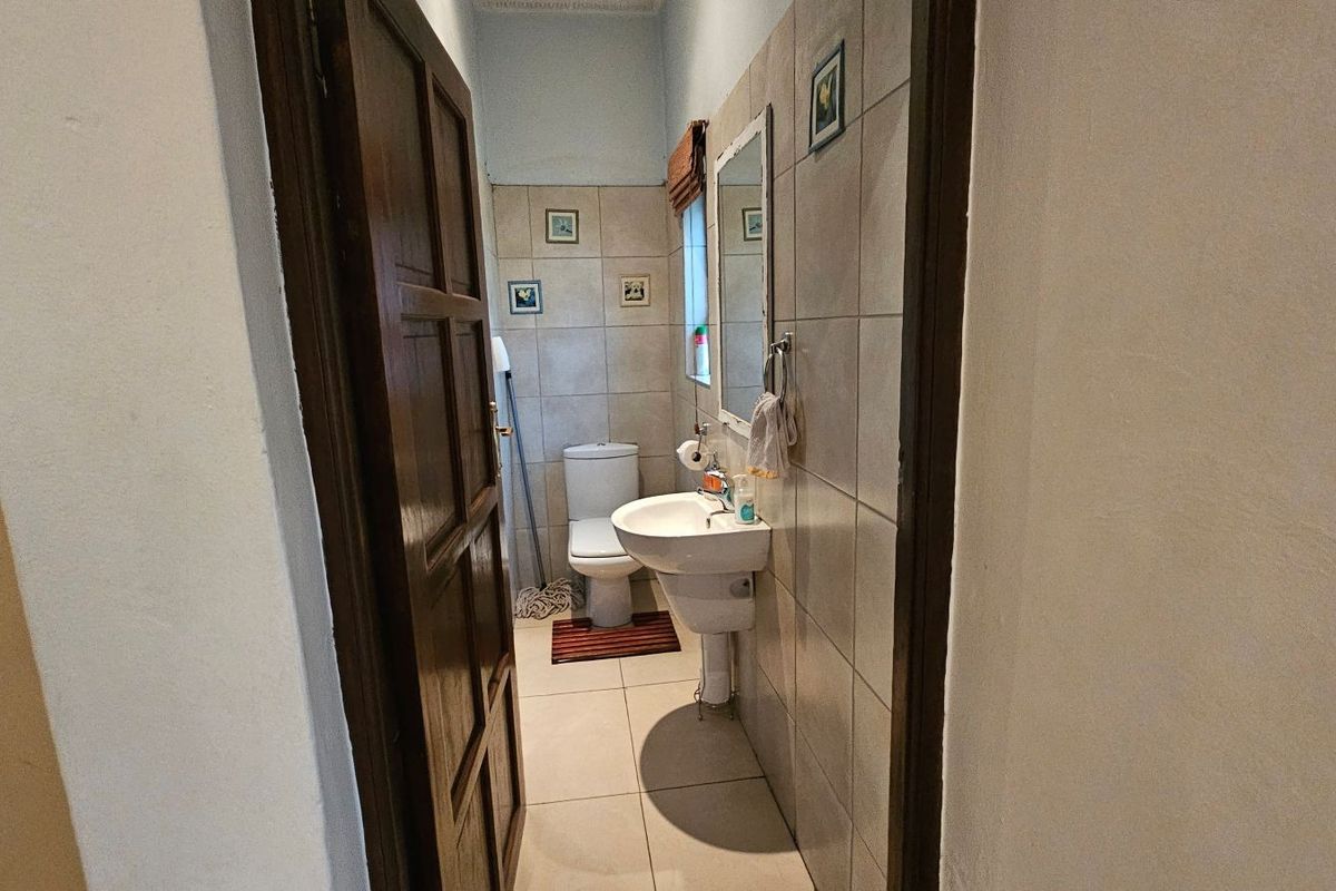 A compact bathroom featuring tiled walls and flooring, equipped with a pedestal basin and a standard toilet.