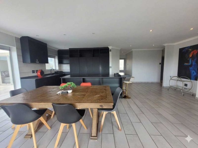 Spacious open-plan living area featuring a modern kitchen with dark cabinetry, a central island, and tiled flooring, seamlessly connecting to the dining space.