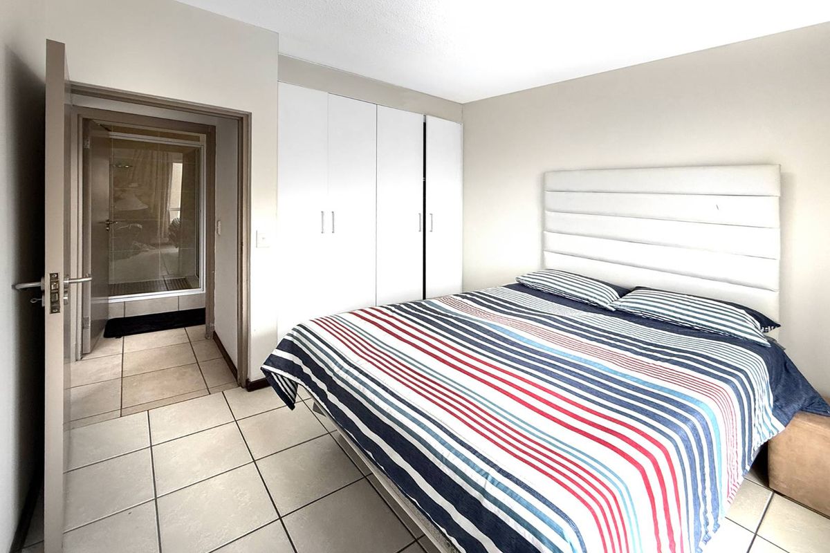 A bedroom featuring tiled flooring and built-in white cabinetry, with an adjoining bathroom visible through the doorway.