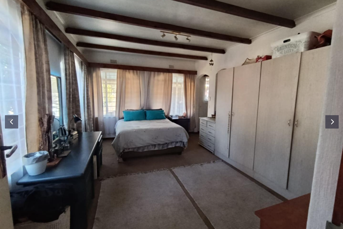 Spacious bedroom featuring exposed timber ceiling beams, built-in cupboards, and carpeted flooring, offering a comfortable and functional living space.