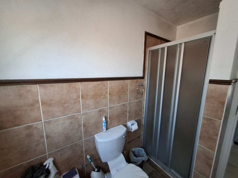 A functional bathroom featuring a shower enclosure and toilet with partial wall tiling, requiring cosmetic updates to modernize the space.