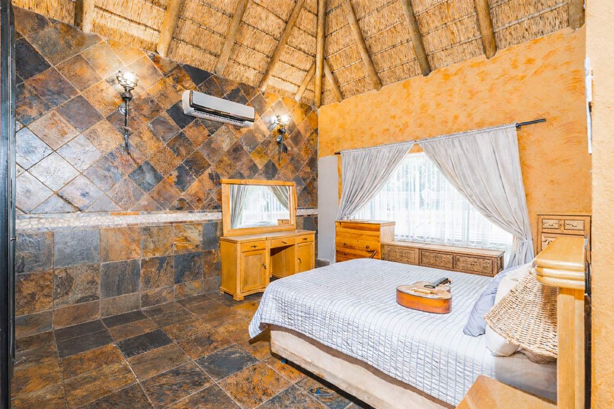 A rustic bedroom featuring a high thatched ceiling, slate tile wall cladding, and a wall-mounted air conditioning unit.