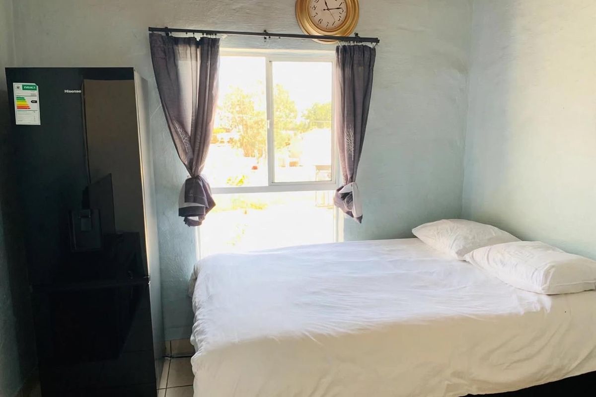 A bedroom featuring tiled flooring and a sliding window, showing signs of wear on the wall finishes.
