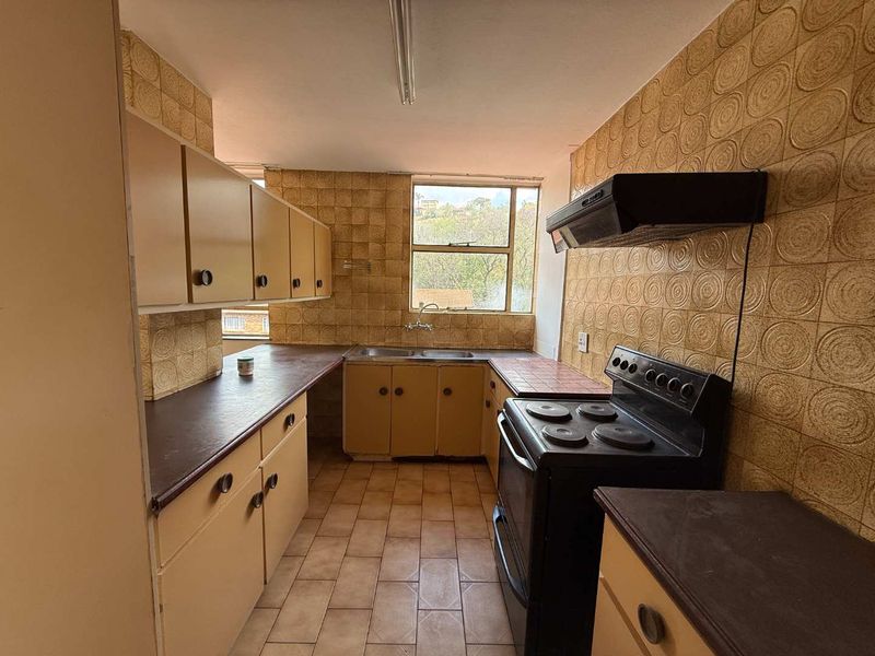 A dated kitchen featuring original cabinetry, tiled backsplash, and a freestanding stove, offering significant potential for a modern renovation.