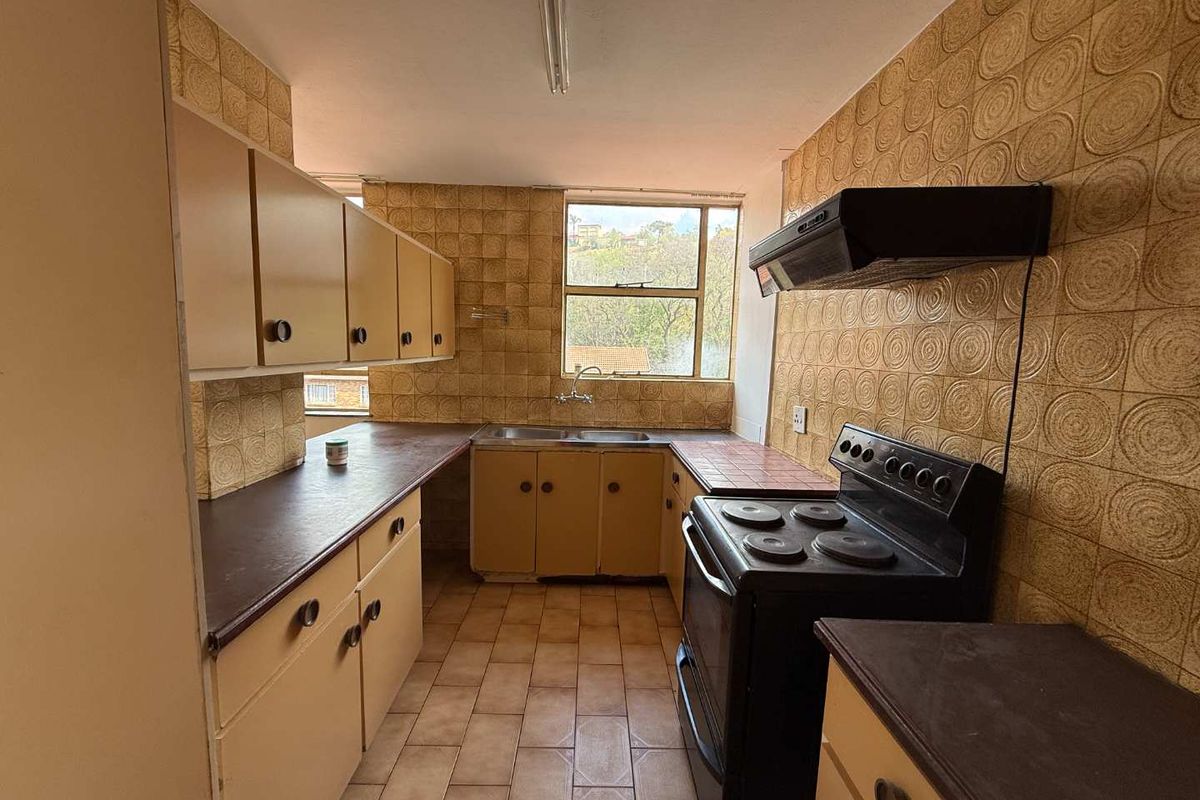 A dated kitchen featuring original cabinetry, tiled backsplash, and a freestanding stove, offering significant potential for a modern renovation.