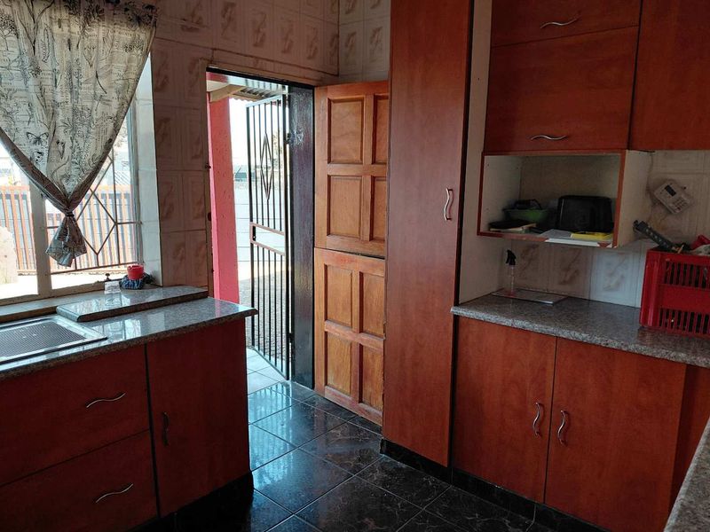 A functional kitchen featuring wood-look laminate cabinetry, granite countertops, tiled backsplash, and direct access to an outdoor area via a security gate.