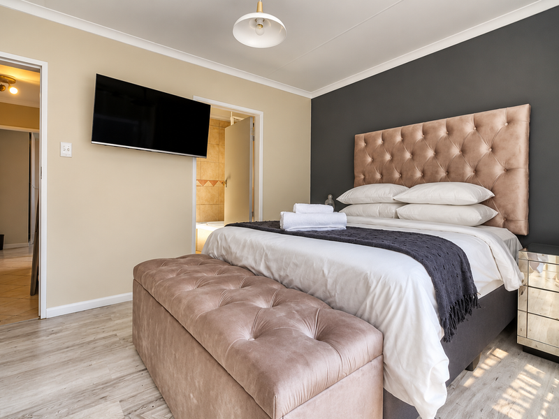 A well-maintained bedroom featuring laminate flooring, a feature wall, and an en-suite bathroom access.