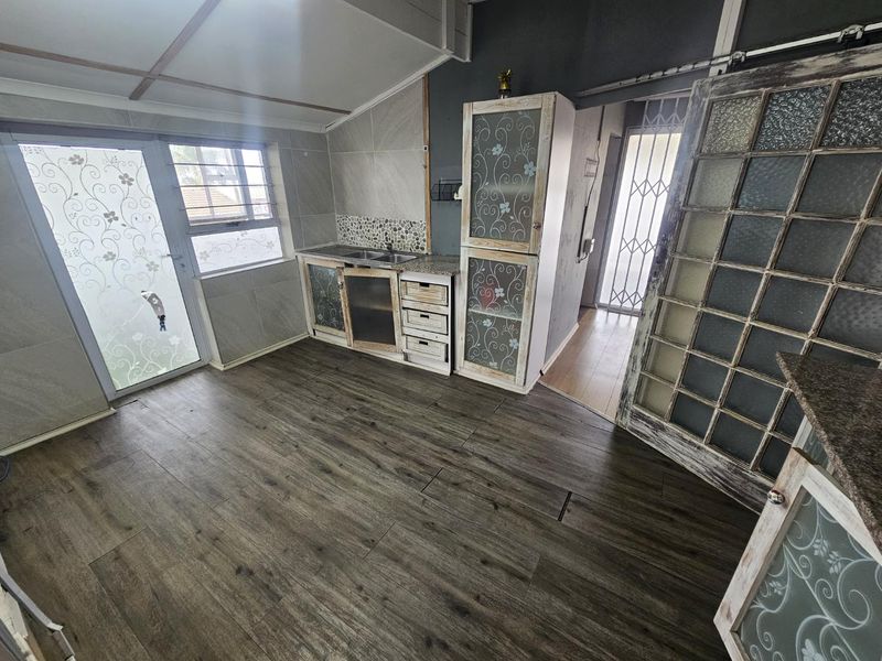A compact kitchen area featuring built-in cabinetry, a stainless steel sink, tiled splashbacks, and wood-look laminate flooring with direct access to the exterior.