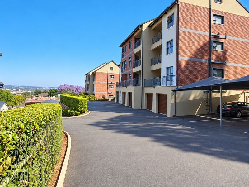 Exterior view of a modern apartment complex featuring brick facades, private balconies, covered parking bays, and well-maintained landscaped grounds.