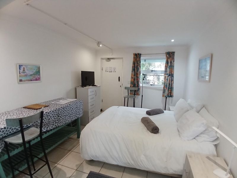 A functional bedroom featuring tiled flooring, a window with curtains, and a standard entry door.