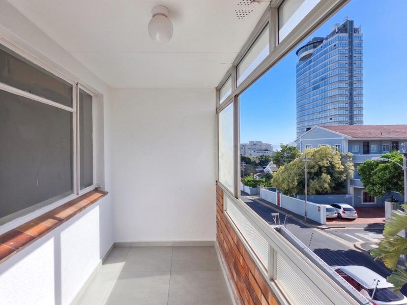 An enclosed balcony featuring tiled flooring and large windows, offering an elevated urban view of the surrounding neighborhood and city skyline.