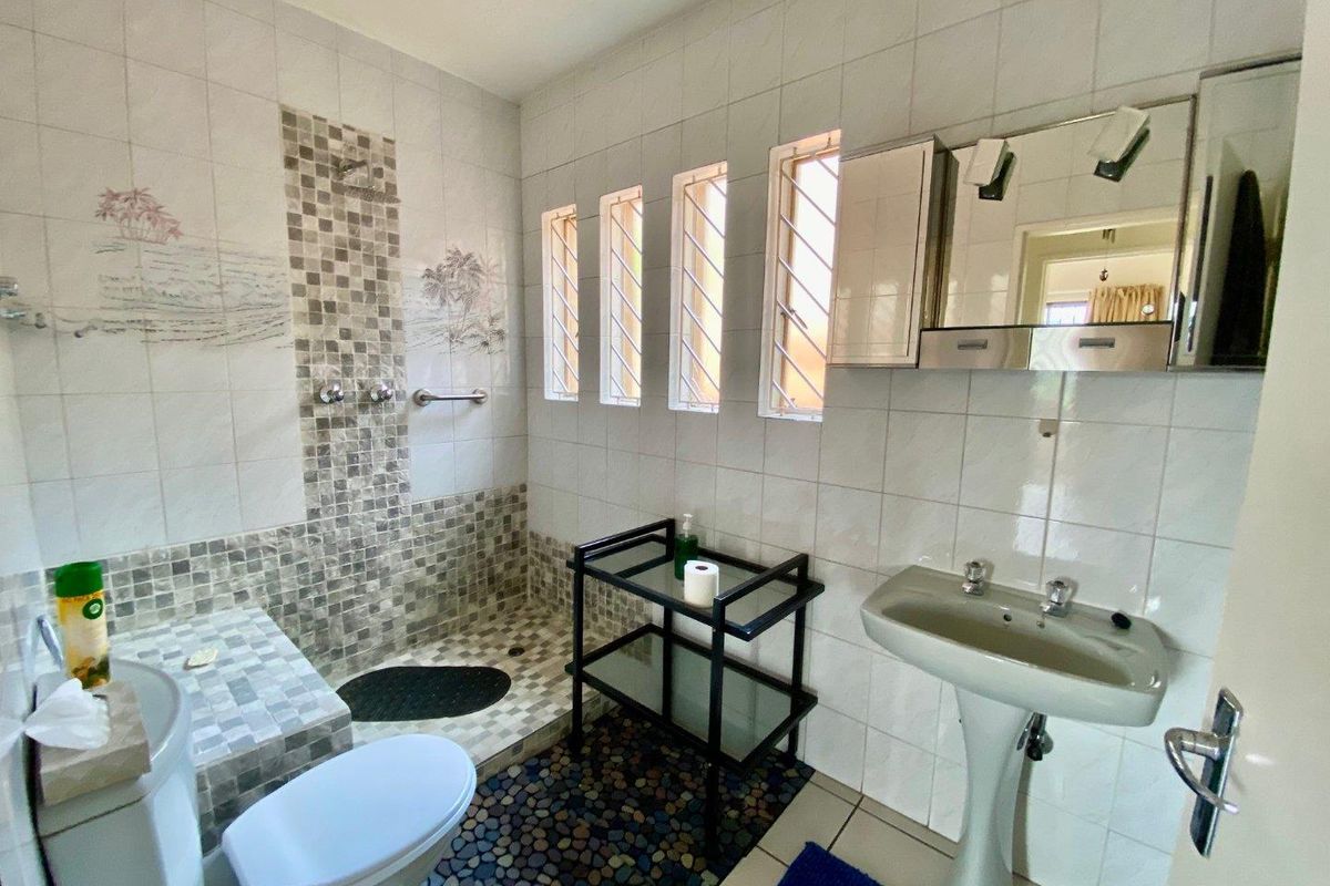 A functional bathroom featuring a tiled shower area, pedestal basin, and wall-mounted medicine cabinet with integrated lighting.