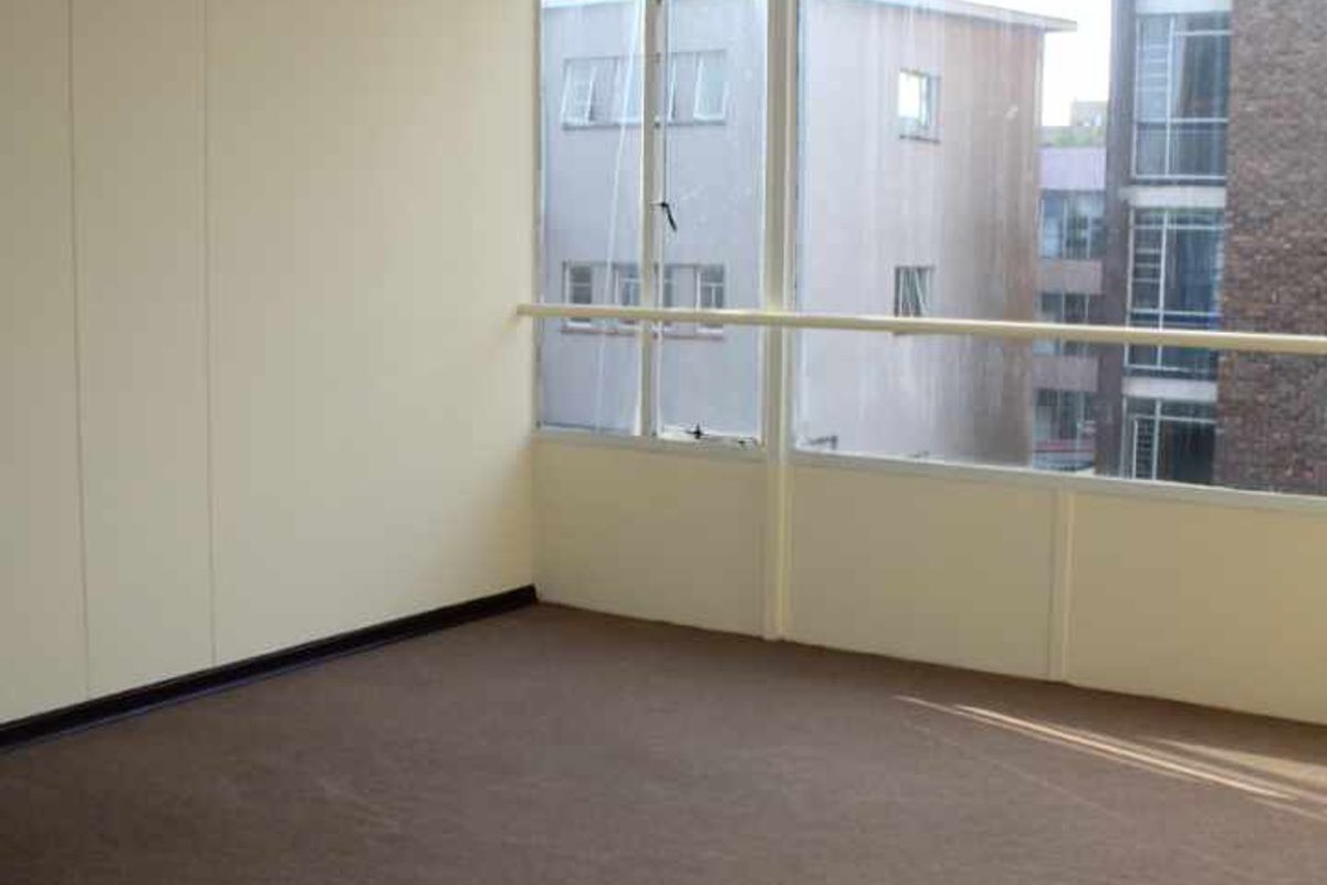 An empty living room featuring large windows, carpet flooring, and a simple ceiling light fixture, offering a blank canvas for potential updates.