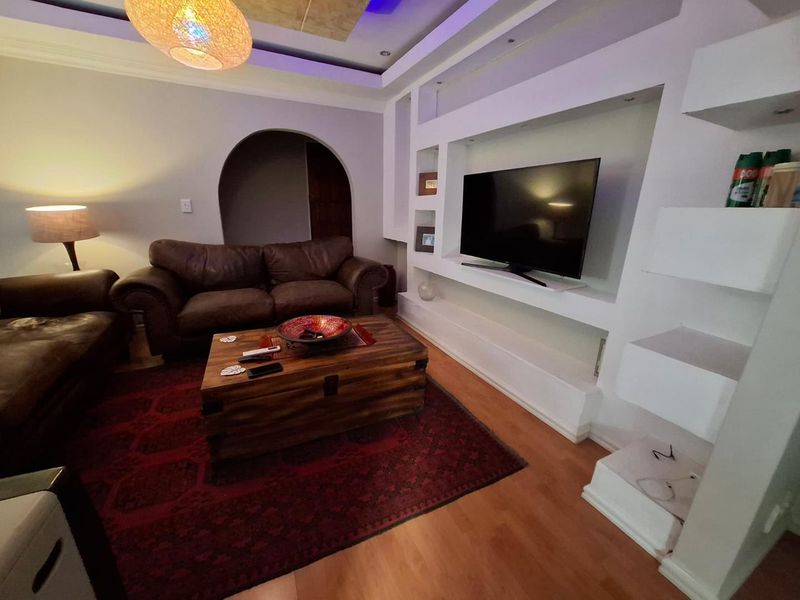 A living room featuring a built-in media wall with shelving, recessed ceiling lighting, and laminate flooring, accessed through a classic archway.
