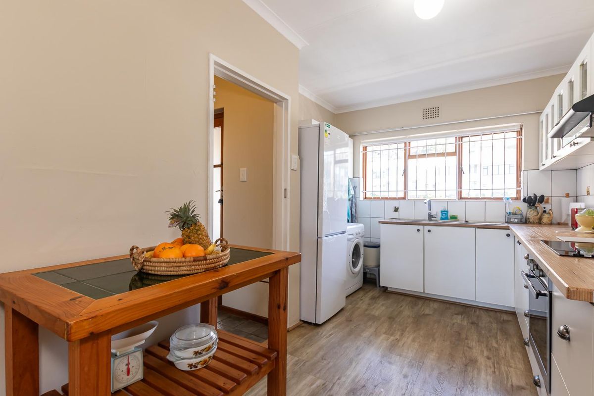 Functional kitchen featuring white cabinetry, wood-look countertops, integrated oven and hob, and a dedicated laundry area with plumbing for a washing machine.