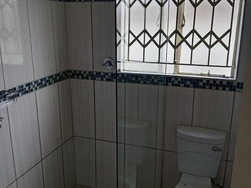 A functional bathroom featuring a walk-in shower with a glass screen, tiled walls with decorative accents, and a standard toilet.