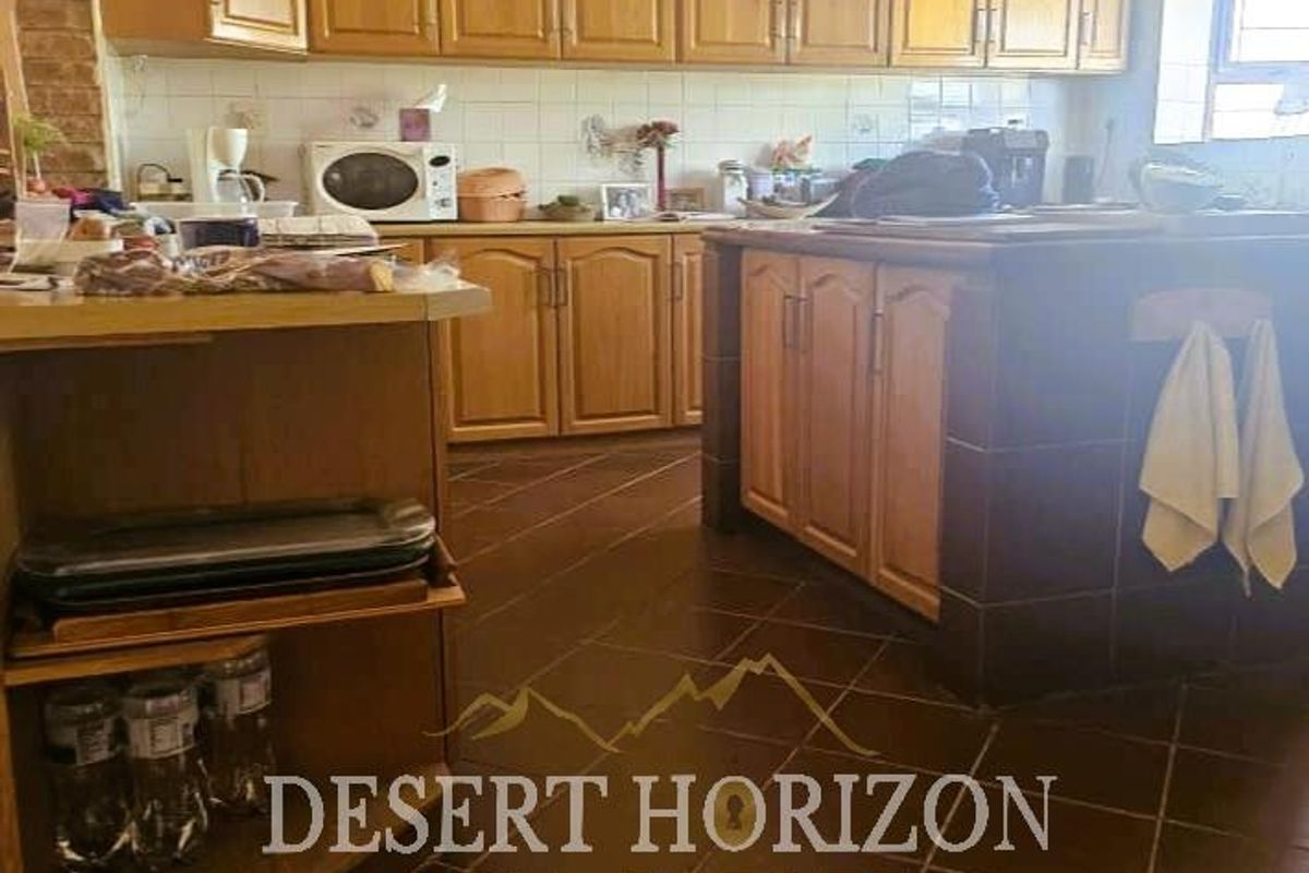 A functional kitchen featuring wooden cabinetry, tiled countertops, and dark floor tiles, offering a traditional layout with ample storage space.
