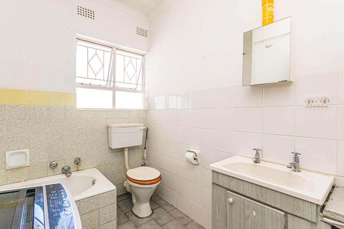 A dated bathroom featuring a built-in bathtub, a standard toilet, and a vanity basin with tiled walls and flooring.