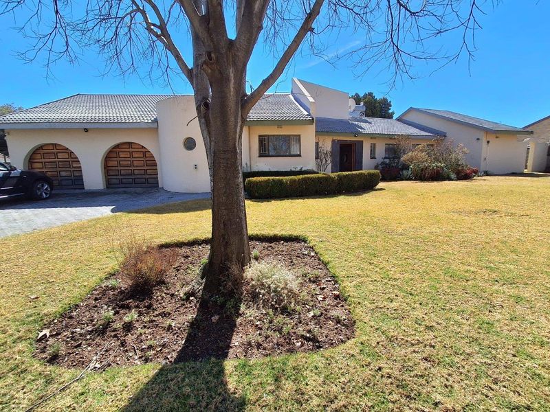 Front elevation of a single-story house featuring a double garage with arched doors, a paved driveway, and a well-maintained front garden.