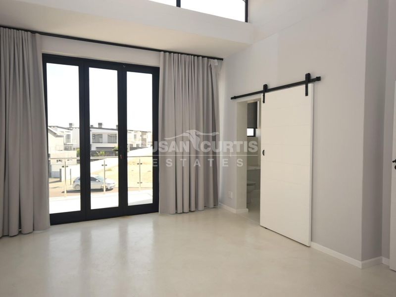 Spacious bedroom featuring double-volume ceilings, polished concrete floors, and a modern sliding barn door leading to an en-suite bathroom.