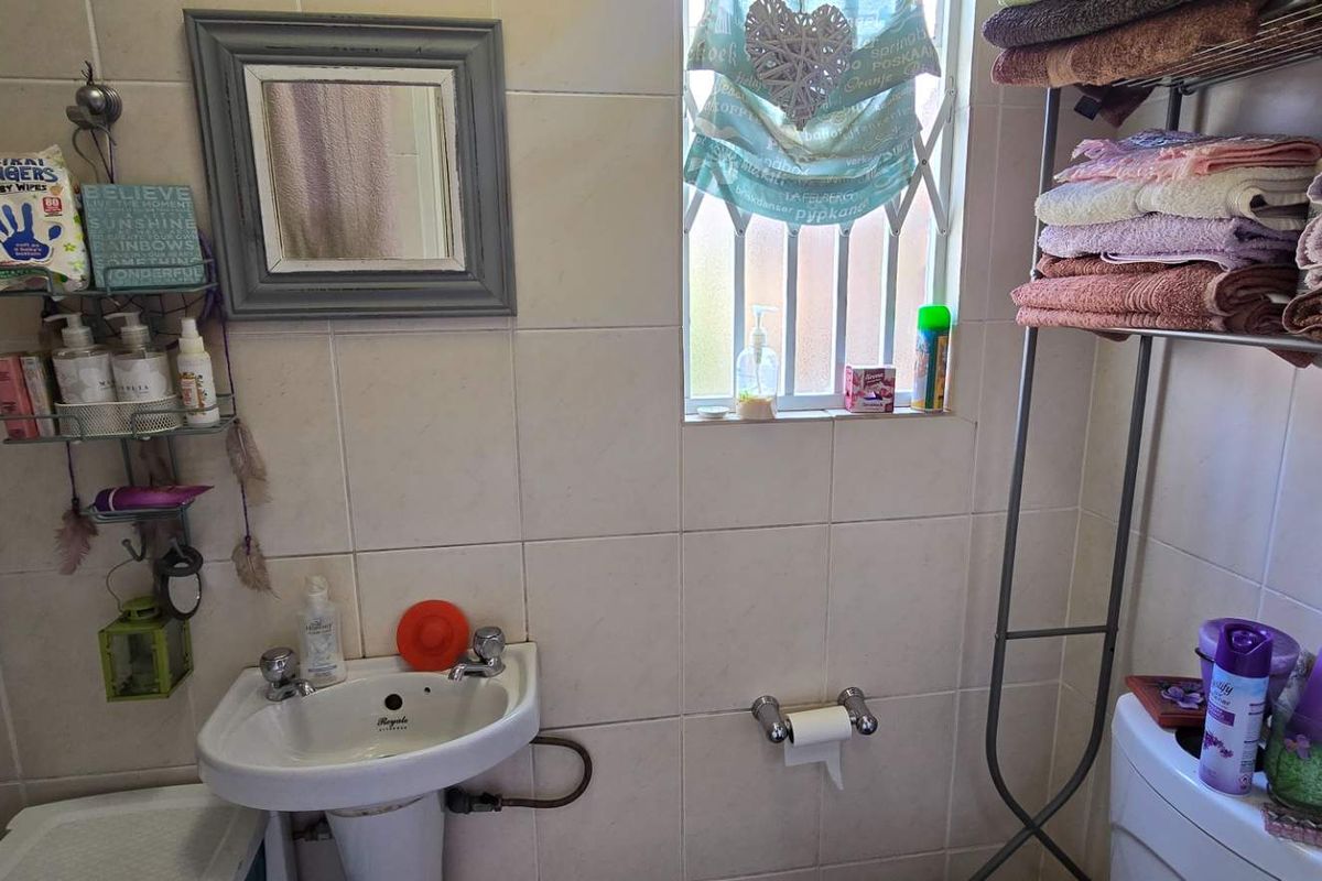 A compact bathroom featuring a pedestal washbasin, tiled walls, and a window with a security gate.