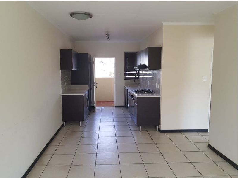 A functional galley-style kitchen featuring dark cabinetry, gas hob, extractor fan, and tiled flooring, leading directly to an outdoor balcony area.