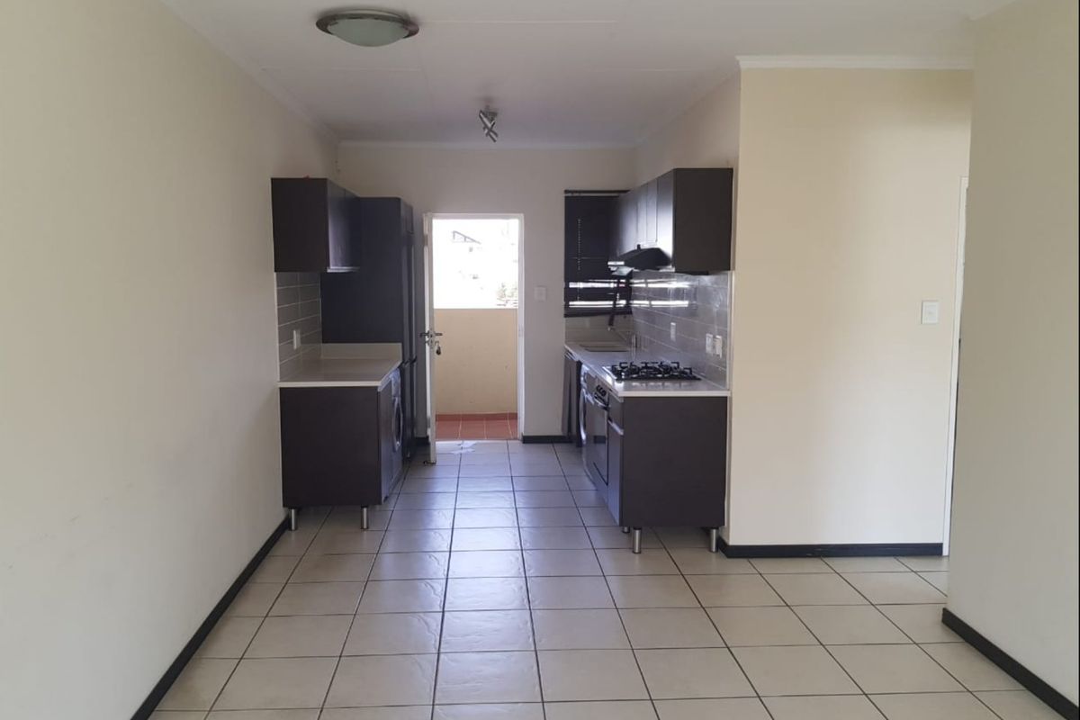 A functional galley-style kitchen featuring dark cabinetry, gas hob, extractor fan, and tiled flooring, leading directly to an outdoor balcony area.
