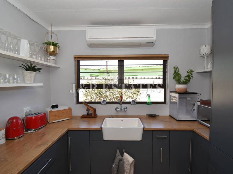 Modern kitchen featuring dark cabinetry, wooden countertops, a farmhouse-style sink, and a wall-mounted air conditioning unit.