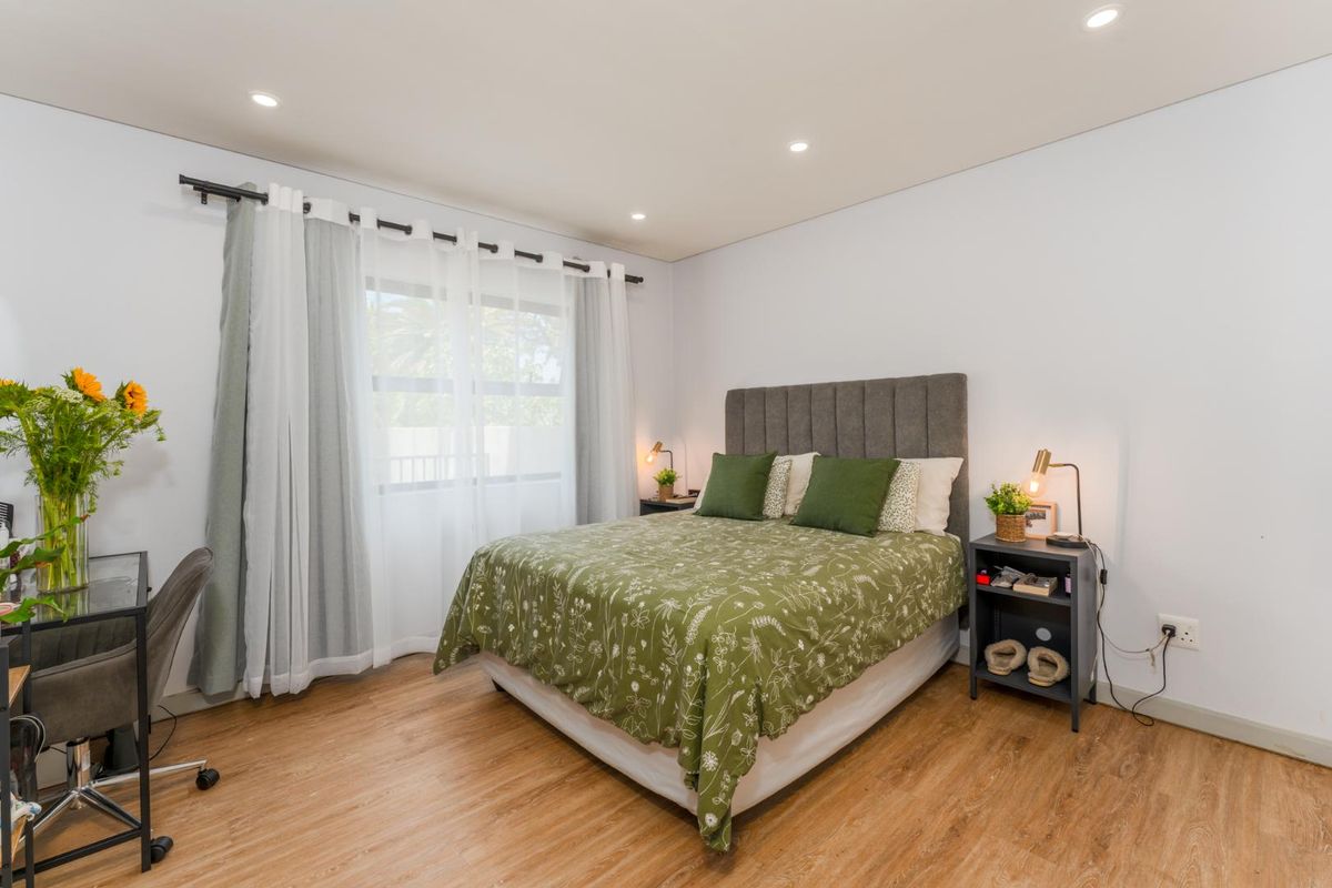 A well-maintained bedroom featuring laminate flooring, recessed downlighting, and a large window with installed curtain rods.