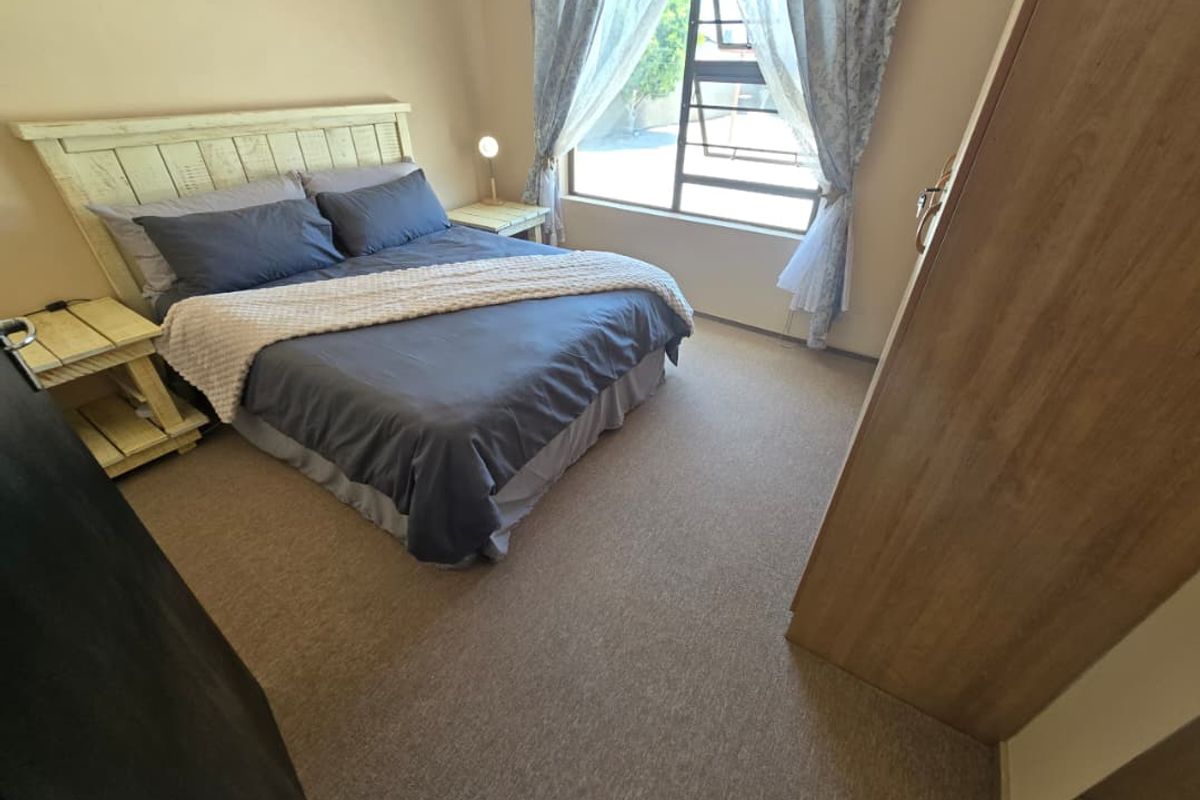A functional bedroom featuring neutral carpeting, a large window with natural light, and built-in cabinetry.