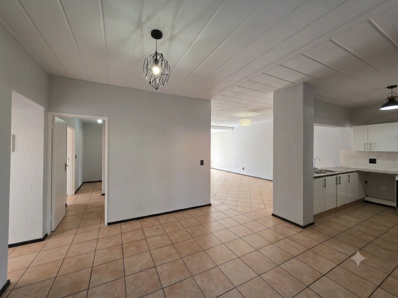 Spacious open-plan living and kitchen area featuring neutral tiled flooring, built-in cabinetry, and modern pendant lighting throughout the bright, vacant interior space.