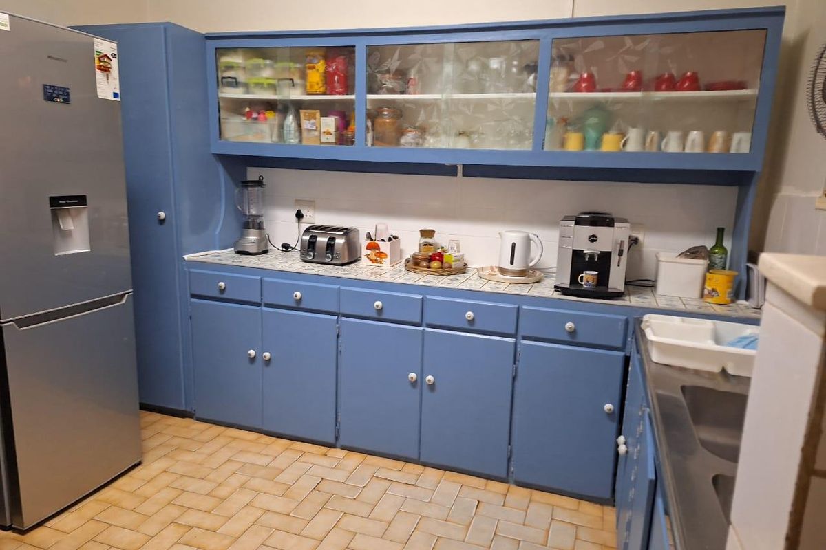 A functional kitchen featuring blue built-in cabinetry, tiled countertops, and a stainless steel sink, offering potential for a modern cosmetic update.