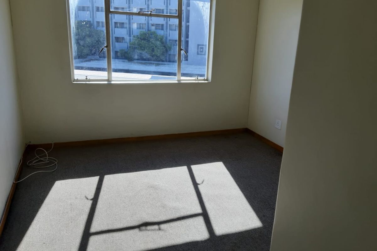 An empty bedroom featuring carpet flooring and a window with natural light, providing a blank canvas for potential interior design updates.