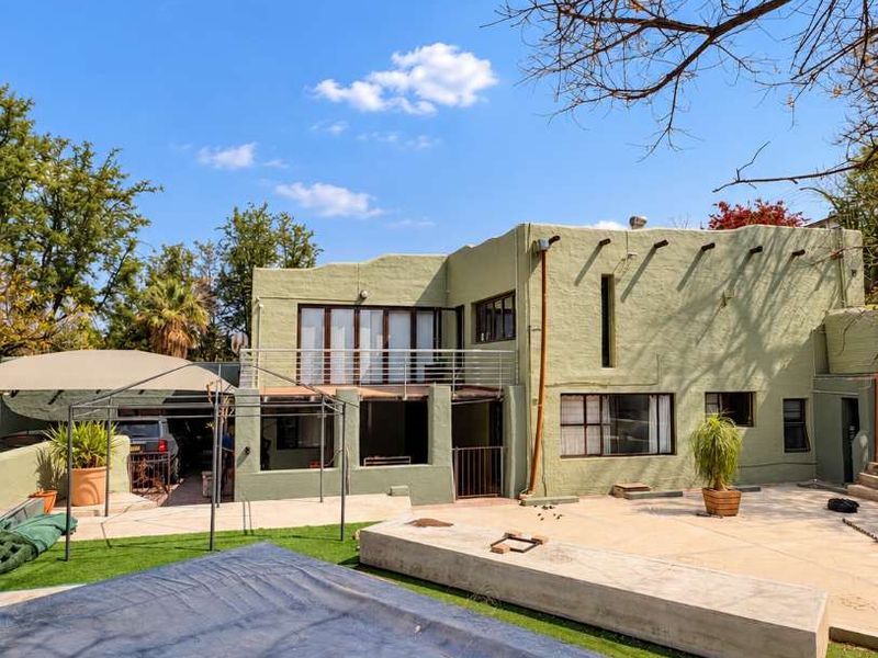 Rear exterior view of the property featuring a swimming pool, paved patio area, artificial lawn, and a balcony overlooking the garden.