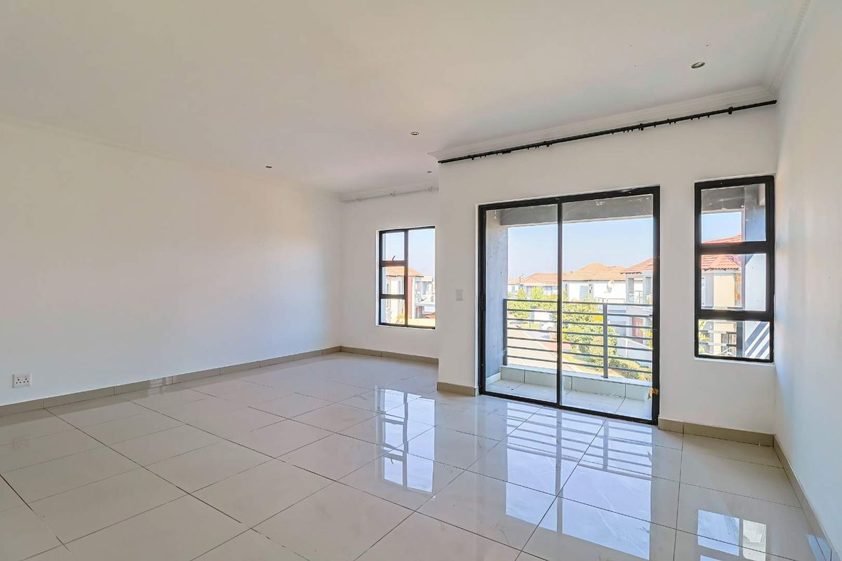 A bright, spacious, and empty living area featuring large tiled floors, recessed lighting, and a sliding glass door leading to a private balcony.