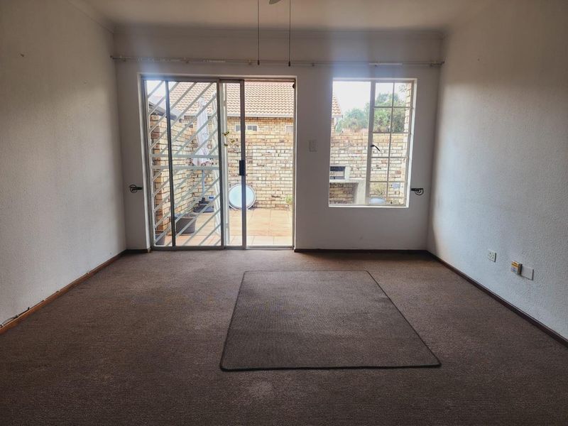 An empty living room featuring carpet flooring, a sliding glass door with security gate, and a window overlooking a private rear courtyard.