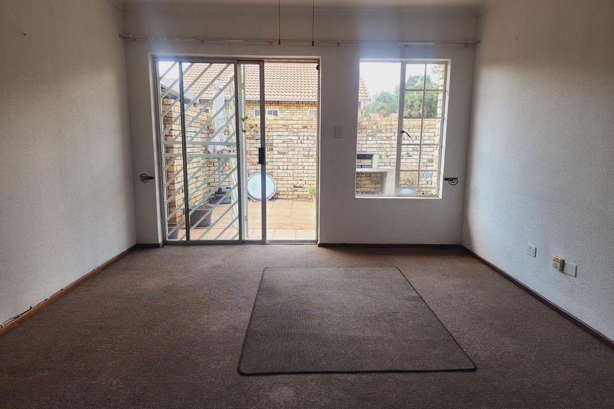 An empty living room featuring carpet flooring, a sliding glass door with security gate, and a window overlooking a private rear courtyard.