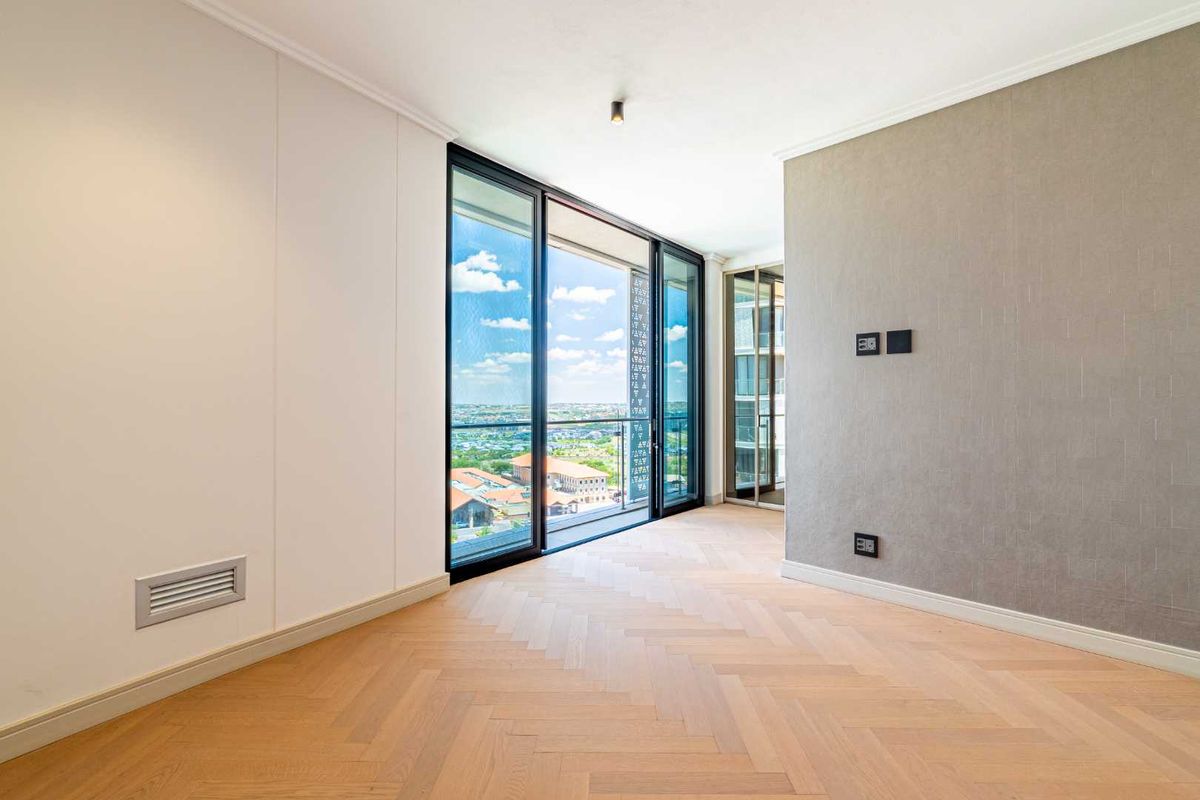Bright and modern living space featuring elegant herringbone timber flooring, floor-to-ceiling glass sliding doors, and access to a private balcony with expansive views.