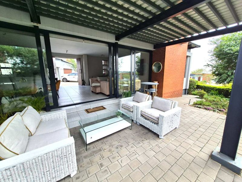 A covered outdoor patio featuring paved flooring, a brick accent wall, and large sliding glass doors providing seamless access to the interior living space.
