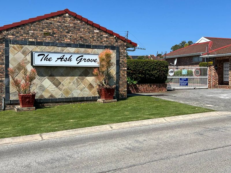 Front entrance view of The Ash Grove townhouse complex, featuring a brick and stone facade, security gate, and well-maintained lawn.