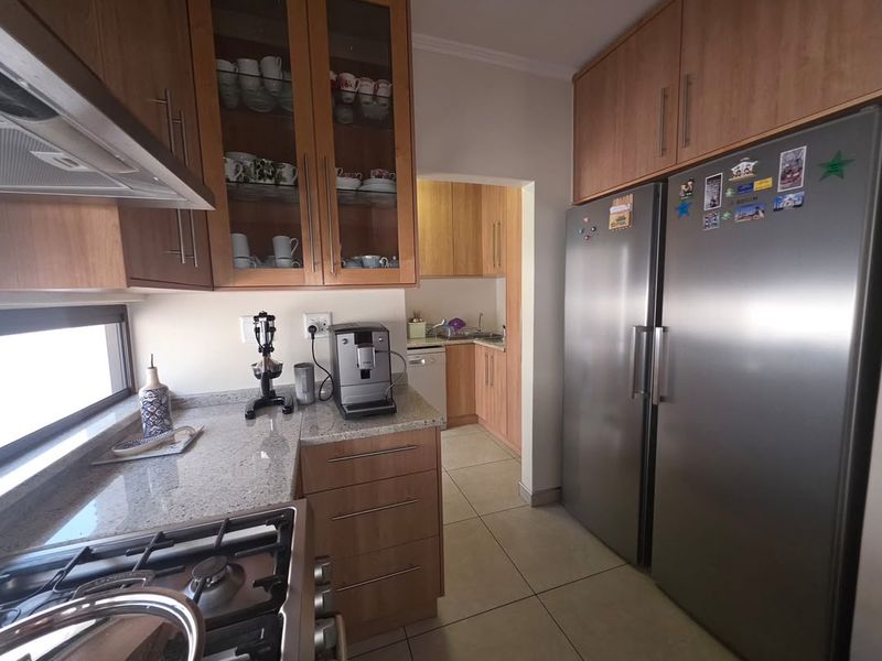 A functional kitchen featuring wooden cabinetry, granite countertops, a gas hob with extractor, and an adjoining scullery area with tiled flooring throughout.