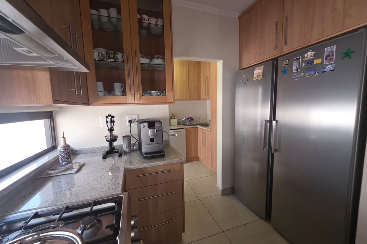 A functional kitchen featuring wooden cabinetry, granite countertops, a gas hob with extractor, and an adjoining scullery area with tiled flooring throughout.