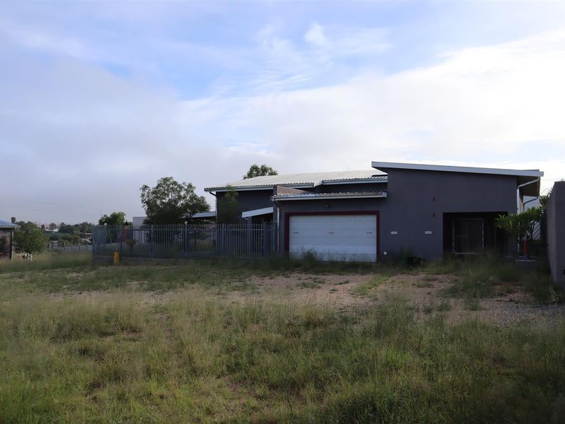 Front exterior view of a mixed-use property featuring a garage, metal fencing, and a large unmaintained yard area.