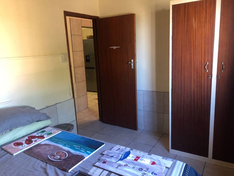 A bedroom featuring tiled flooring and a built-in wooden wardrobe, with an adjoining doorway leading to another room.